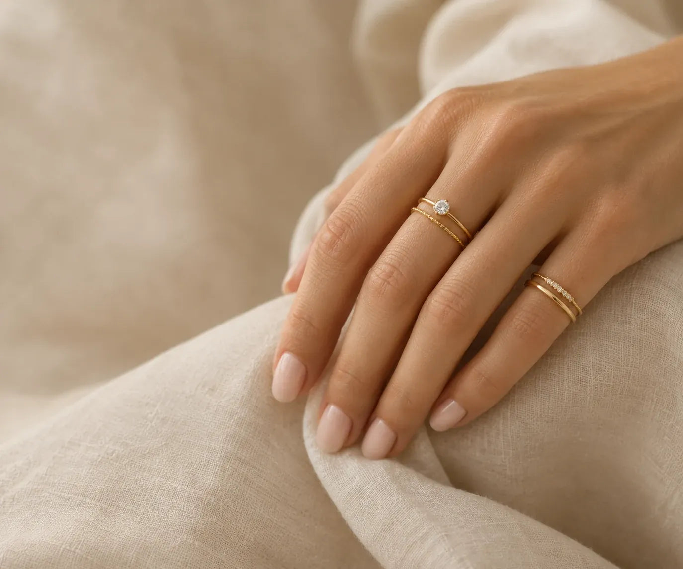 Hand wearing stacked gold rings on linen